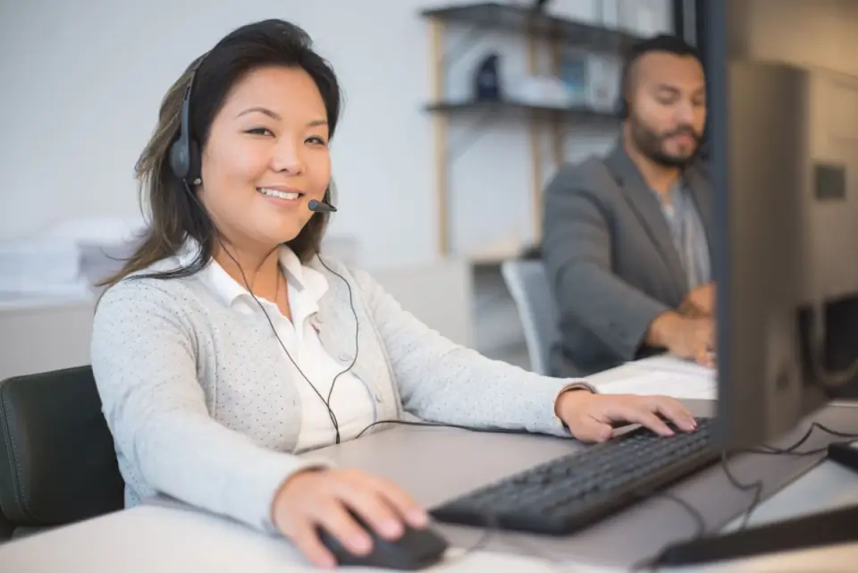 Atendente sorrindo com fone de ouvido em frente ao computador